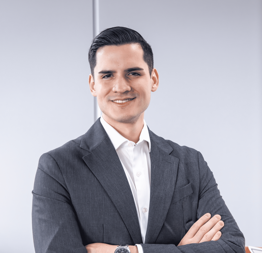 Professional man in a gray suit with a white shirt, arms crossed, smiling at the camera.